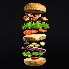 Papier Peint photo Pour lui Burger flottant isolé sur fond en bois noir. Ingrédients d& 39 un délicieux hamburger avec galette de boeuf haché, laitue, bacon, oignons, tomates et concombres