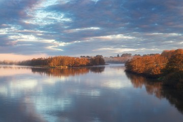 Naklejka na ściany i meble Dawn in a fog on the river. Autumn morning. A fog over water. The sun in a fog. Early morning sunrise glow and rising mist over the Waikato river in North island