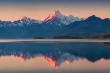 Fototapeta na wymiar Snowy mountain range reflected in the still water of Lake Pukaki, Mount Cook, South Island, New Zealand. The turquoise water comes from Mt. Cook and Tasman glacier. Popular travel destination 