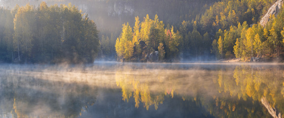 Naklejka na ściany i meble Autumn forest reflected in water. Colorful autumn morning in the mountains. Colourful autumn morning in mountain lake. Foggy autumn sunrise. Beautiful autumn background concept.