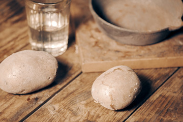 on the table raw potatoes. a glass of water, an empty iron old frying pan. concept of hunger