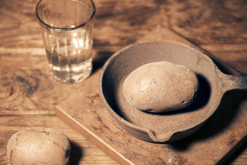 on the table raw potatoes. a glass of water, an empty iron old frying pan. concept of hunger