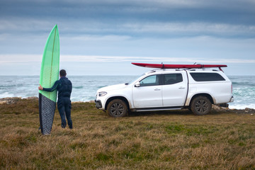 surfista con una tabla de olas gigantes en frente del mar y vehículo todoterreno con una tabla de surf encima en frente del mar © marcantabrico