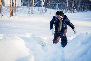Fototapeta na wymiar A boy with a white dog Spitz walks in winter in the snow