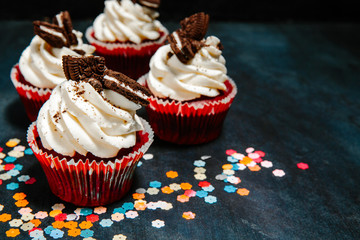 beautiful Cupcakes with cream and cookies on a black background and confetti