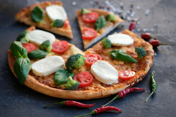 Sliced pizza with Mozzarella cheese, tomatoes, broccoli, Spices and fresh basil. Italian pizza. Pizza on black stone background
