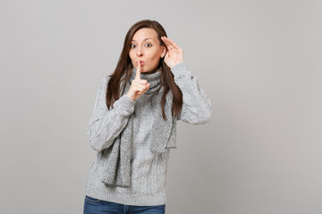 Young girl in gray sweater scarf saying hush be quiet with finger on lips shhh gesture eavesdrop...