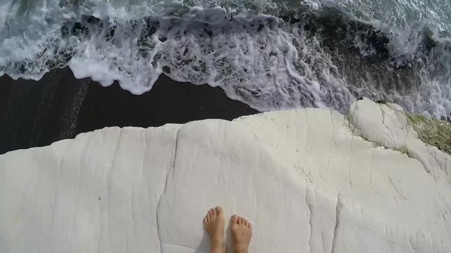 Woman feet on white rock on famous Governor's beach with black sand, landmark of Cyprus. POV, slow motion.