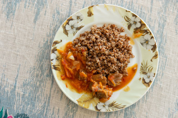 Top view on a plate with cooked buckwheat and sauced pork meat standing on a tablecloth