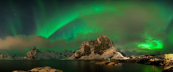 Aurora borealis dancing on mountain in fishing village at Reine and Sakrisoy, Lofoten, Norway...