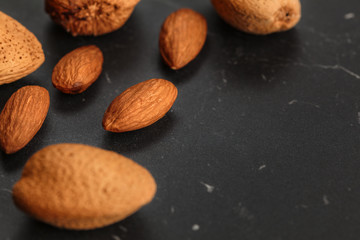 Closeup of almonds, both peeled and whole, on dark board. Space for text on right side.