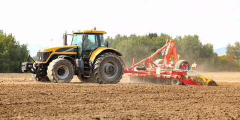 Tractor pulling ploughing / sowing trailer over dry field.
