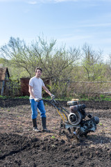 Man with cultivator ploughs ground. Land cultivation, soil tillage. Spring work in the garden. Gardening concept