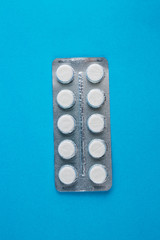 White round pills in pack. Tablets are next to the packaging on a blue background