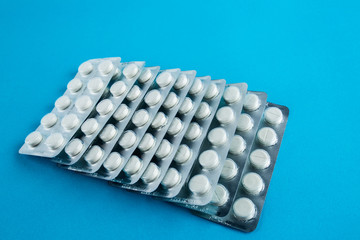 White round pills in pack. Tablets are next to the packaging on a blue background