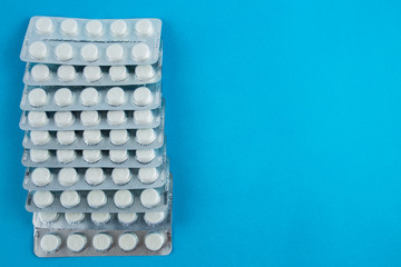 White round pills in pack. Tablets are next to the packaging on a blue background