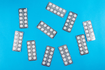 White round pills in pack. Tablets are next to the packaging on a blue background