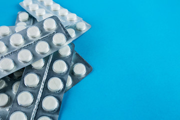 White round pills in pack. Tablets are next to the packaging on a blue background