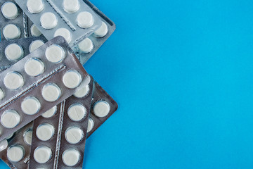 White round pills in pack. Tablets are next to the packaging on a blue background