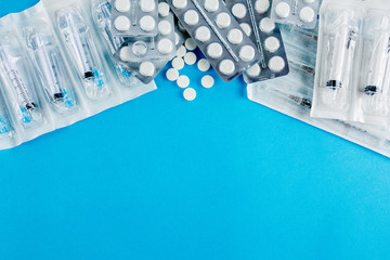 packs of white pills and syringes on a blue background