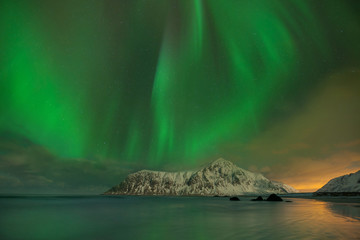 Fototapeta na wymiar Aurora Borealis on the Lofoten Islands, Norway. Green northern lights above mountains and beach. Night sky with polar sky above arctic circle. Winter landscape with aurora reflection on the water.