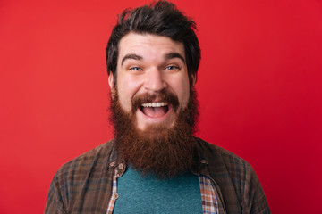 Portrait of an excited bearded man with open mouth isolated over red background