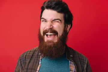 Obraz premium A handsome young bearded man doing flirting gesture with eye over red background
