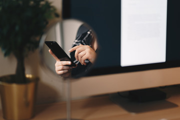 creative shot of a woman's hands typing on a cellphone in the reflection of a makeup mirror. home office like space.