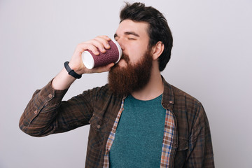 Fototapeta na wymiar Handsome brunette bearded man drinks coffee over gray background