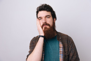 Fototapeta premium Very bored adult man with beard holding hand on cheek while support it with another crossed hand.