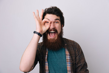 Handsome man with blue eyes and beard  doing ok gesture shocked with surprised face, eye looking through fingers.