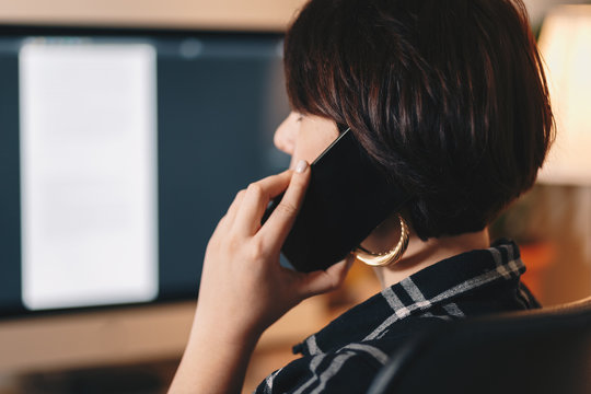 independent businesswoman working from a home office, private workspace, talking on a cellphone. face hidden from the camera