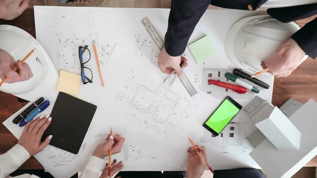 large work table on which are glasses, phone, markers, pencils, rulers. Hands of designers make amendments to the drawings