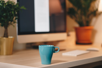 Coffee cup on a wooden table, in front of the working computer. Home office concept, personal working space.