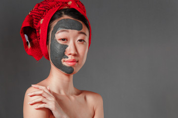 attractive young korean girl with a red towel on her head applied a useful clay mask