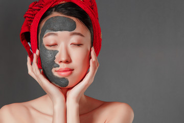 attractive young korean girl with a red towel on her head applied a useful clay mask
