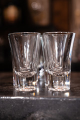 Two rows of empty clean vodka glasses on the black bar of the restaurant