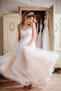 Beautiful bride blonde woman sitting near vintage wardrobe full of wedding dresses. fashion beauty portrait 