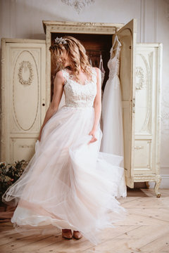 Beautiful bride blonde woman sitting near vintage wardrobe full of wedding dresses. fashion beauty portrait 