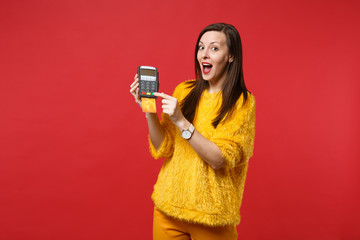 Excited young woman in yellow fur sweater hold wireless modern bank payment terminal to process and acquire credit card payments isolated on red background. People sincere emotions, lifestyle concept.