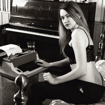 young beautiful woman typing on a retro typewriter. female writer in bra and men's trousers. black and white