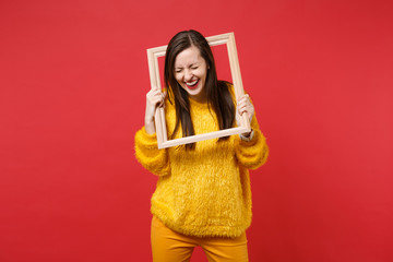 Portrait of laughing young woman in yellow fur sweater with closed eyes holding picture frame...