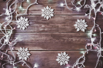 Christmas decor. White snowflakes and garland with glowing lamps on wooden background.