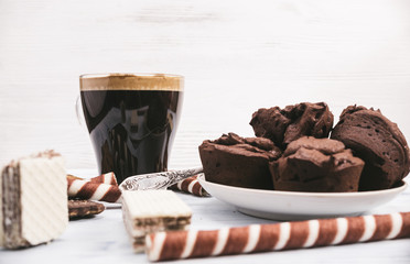 Chocolate muffins and coffee in a glass mug are photographed on a light wooden background.