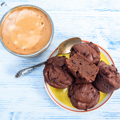 Chocolate muffins and coffee in a glass mug are photographed on a light wooden background.