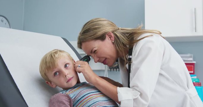 Woman pediatrician performing checking ears of young boy in clinic exam room. female doctor giving exam using otoscope to child in pediatrician office. Slow motion 4k