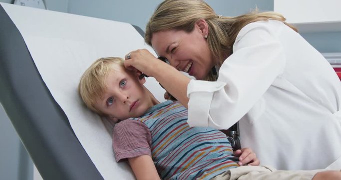 Woman doctor giving exam using otoscope to child in pediatrician office. Female pediatrician checking ears of young boy in clinic exam room. Slow motion 4k