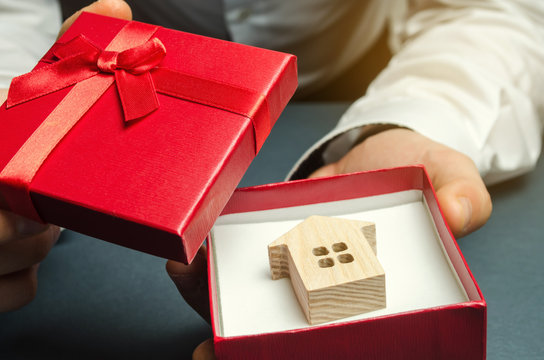 Man holds a miniature house in a gift box. Housing as a gift. Win an apartment in the lottery. To inherit property. Holiday discounts. Buying an apartment at a low price. Sale of real estate. Present