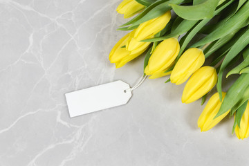 Yellow tulips on a marble background with a blank tag. Romantic/ sale/ spring mock up.