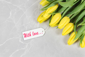 Yellow tulips on a marble background with a tag "with love". Romantic background.